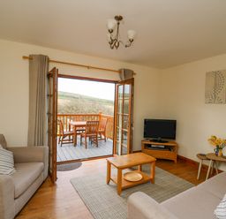 A living room with two sofas a coffee table a TV on a stand and an open door leading to a balcony with a table and chairs at Llaethdy in Cardigan