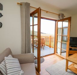 A living room with a sofa a coffee table and a television near open double doors leading to a deck with wooden furniture at Llaethdy in Cardigan