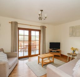 A living room with two sofas a wooden coffee table television and glass doors leading to a balcony at Llaethdy in Cardigan