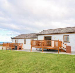 An outdoor view of a white house with two wooden decks and a grassy lawn at Llaethdy in Cardigan