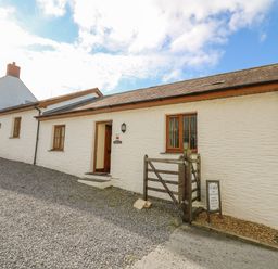 A white exterior building with wooden windows a wooden gate and a gravel driveway at Beudy in Mwnt Cardigan Ceredigion