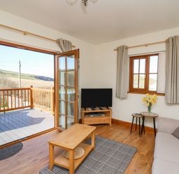 A living room with a sofa a coffee table a tv on a stand and an open door leading to a balcony at Beudy in Mwnt Cardigan Ceredigion
