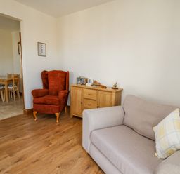 A living room with a red armchair beige sofa wooden sideboard and a floor lamp at Beudy in Mwnt Cardigan Ceredigion