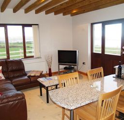 A living room with a brown leather sofa a small coffee table a television and a dining table with wooden chairs at Cable Cottage in Fishguard Pembrokeshire