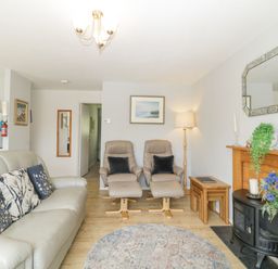 A living room with a sofa and armchairs next to a fireplace with flowers on the floor at 9 Manorcombe Bungalows St Ann's Chapel near Callington
