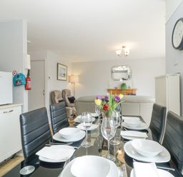 A dining table set with plates glasses and cutlery in an open plan living room with chairs a sofa a mirror and a clock at 9 Manorcombe Bungalows in St Ann's Chapel near Callington