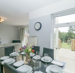 A dining table set with plates glasses and napkins near a sliding door leading to a garden at 9 Manorcombe Bungalows in St Ann's Chapel near Callington