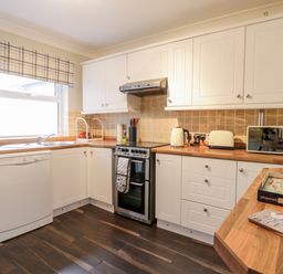 A kitchen with white cabinets dishwasher stove kettle toaster and microwave at Scarborough Cottage in Driffield