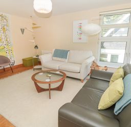 A living room with two sofas a round glass coffee table a patterned wall hanging and large windows at High Banks in Dartmouth