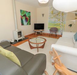 A living room with two sofas a round glass coffee table a small tv a fireplace wooden rocking horse and decorative paintings at High Banks Dartmouth