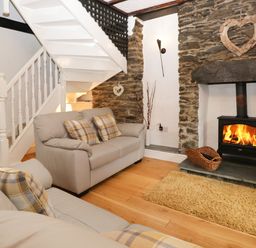 A living room with two sofas a wood burning stove and a staircase at Dalesway Cottage in Bowness-On-Windermere