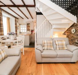 A living room with sofas and plaid pillows next to a staircase and dining table at Dalesway Cottage in Bowness-On-Windermere