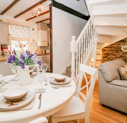 A dining table set with dishes and glasses beside a gray sofa near a white staircase and kitchen at Dalesway Cottage Bowness-On-Windermere