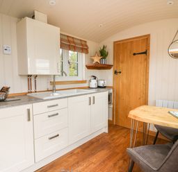 A kitchen with white cabinets a wooden door a small wooden dining table and chairs at Marches Way in Rhayader