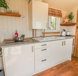 A kitchen with white cabinets a sink a window wooden shelves plants and a wooden door at Marches Way in Rhayader