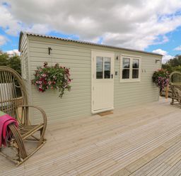 An outdoor deck with two wooden rocking chairs and a small light green cabin with door and window at Marches Way in Rhayader