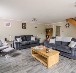 A living room with two sofas a chair a wooden coffee table and a staircase at Byefield Lodge in Welland