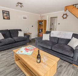 A living room with two gray sofas and a wooden coffee table with a board game and a bottle at Byefield Lodge Welland