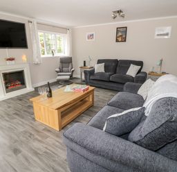 A living room with grey sofas a wooden coffee table and a TV above a fireplace at Byefield Lodge in Welland