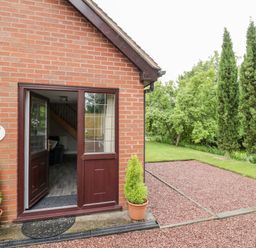 An open wooden door on a brick house showing part of the interior with potted plants outside and green trees at Byefield Lodge in Welland