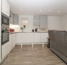 A modern kitchen with white cabinets appliances and a gray sofa at Flat 2 38 Preston Road Weymouth