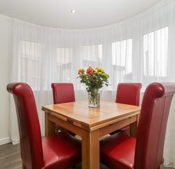 A dining area with a wooden table and four red chairs with a flower vase on the table at Flat 2 38 Preston Road in Weymouth