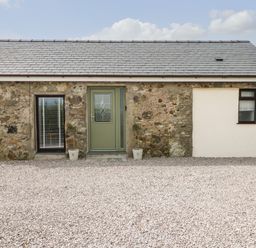 A stone and white exterior wall with a green door and two windows at Tyddyn Haidd in Amlwch