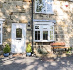 A stone facade with a white door and window beside a wooden bench and potted plants at Parva in Great Broughton near Stokesley