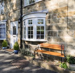 A stone house exterior with white framed windows a white door two potted plants and a wooden bench at Parva in Great Broughton near Stokesley