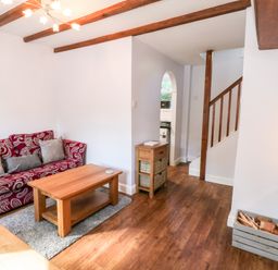 A living room with a red patterned sofa a wooden coffee table a small wooden cabinet and visible stairs at Parva Great Broughton near Stokesley