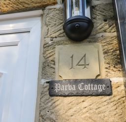 A house number 14 and a sign saying Parva Cottage on a stone wall next to a white door and a black outdoor light at Parva Cottage in Great Broughton near Stokesley