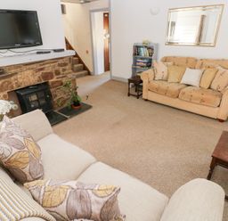A living room with sofas a wall mounted television a stone fireplace and a small bookshelf at Barn Court Cottage Narberth Pembrokeshire