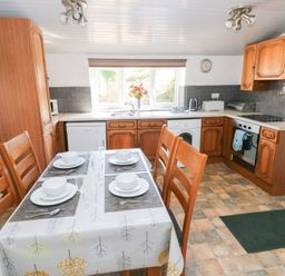 A kitchen with wooden cabinets a dining table set for four and appliances at Barn Court Cottage Narberth Pembrokeshire