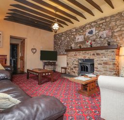 A living room with a stone fireplace a leather sofa a carpet and a television at Stoney Cottage in Narberth Pembrokeshire