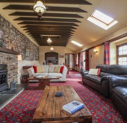 A living room with stone fireplace wooden tables sofas and red patterned carpet at Stoney Cottage Narberth Pembrokeshire