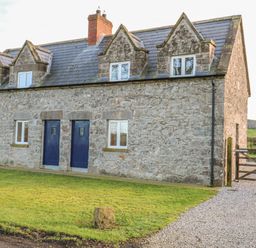 A stone cottage with blue doors and windows and a gravel driveway with a wooden gate at Goose Cottage in Caledon near Killylea