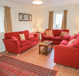 A living room with three red sofas a wooden coffee table two table lamps three framed botanical prints and patterned curtains at Goose Cottage in Caledon near Killylea