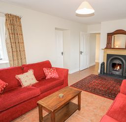 A living room with two red sofas a wooden coffee table a fireplace and patterned curtains at Goose Cottage in Caledon near Killylea