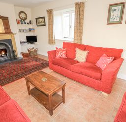 A living room with red sofas a wooden coffee table a fireplace and a small TV at Goose Cottage in Caledon near Killylea