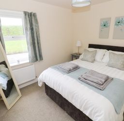 A bedroom with a bed folded towels bedside tables a lamp a window with curtains and a standing mirror at Smugglers in Lydstep