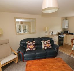 A living room with a black leather sofa with patterned cushions a beige armchair a wooden coffee table and a kitchen area with a dining table at Smugglers in Lydstep