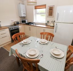 A kitchen with a dining table set for four with plates glasses and cutlery and kitchen appliances including a refrigerator oven microwave kettle and toaster at Smugglers in Lydstep