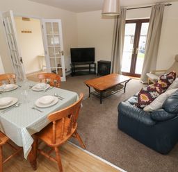 A dining area with a table set for four and a living room with a blue sofa, armchair, coffee table, and television at Smugglers in Lydstep