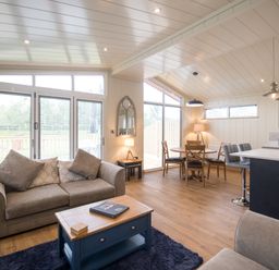 An open living area with a sofa coffee table dining table chairs bar stools and kitchen island at Wren Lodge in Gargrave