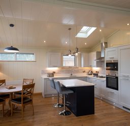 A kitchen with a dining table with four chairs and a kitchen island with two stools at Wren Lodge in Gargrave