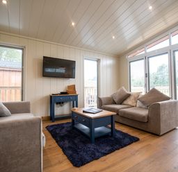A living room with two sofas a coffee table and a TV on the wall at Wren Lodge in Gargrave