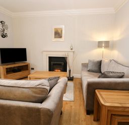 A living room with two sofas a wooden coffee table a fireplace and a television at Tethera in Bowness-On-Windermere