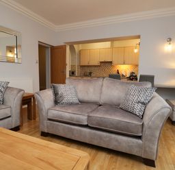 A living room with gray sofas and patterned cushions wooden coffee table and an open kitchen at Tethera in Bowness-On-Windermere