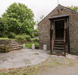 Stone building with wooden stairs and door next to stone steps and trees at Ribby Barn in Lerryn