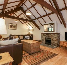 A living room with a wooden beams ceiling a stone fireplace a wooden coffee table two leather sofas a floor lamp and a television at Ribby Barn in Lerryn
